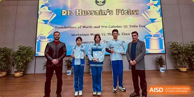 A group of students and adults posing on a stage in front of a banner referencing "Dr. Hussain's Picks" and courses like Math, Pre-Calculus, and Chemistry. Canada British Colombia International Schools-Hefei.