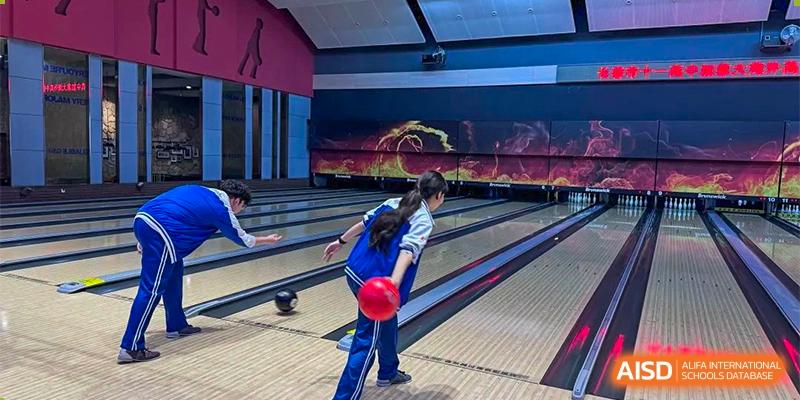 A female student in a blue uniform bowling, throwing a red ball down the lane in an indoor bowling alley. Canada British Colombia International Schools-Hefei.
