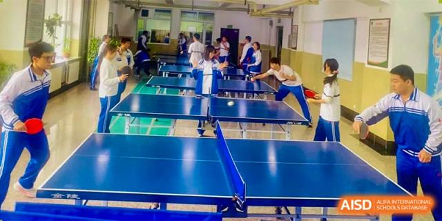 Students engaged in a game of table tennis (ping pong) on a blue table in an indoor setting. Canada British Colombia International Schools-Hefei.