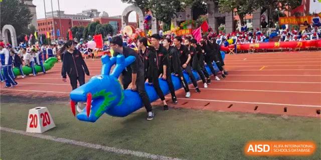 A team of students participating in an outdoor relay race while carrying a large, blue, inflatable object on a red running track. Canada British Colombia International Schools-Hefei.