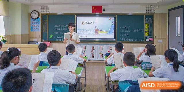A teacher instructs students in a primary classroom at Wuhan Foreign Languages School International Division, using a large digital screen.