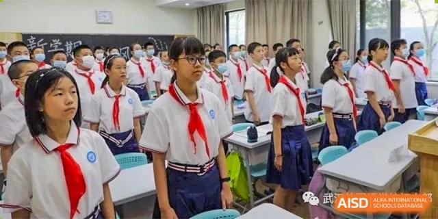 Students from Wuhan Foreign Languages School International Division wearing red scarves and standing attentively in class or during an assembly.