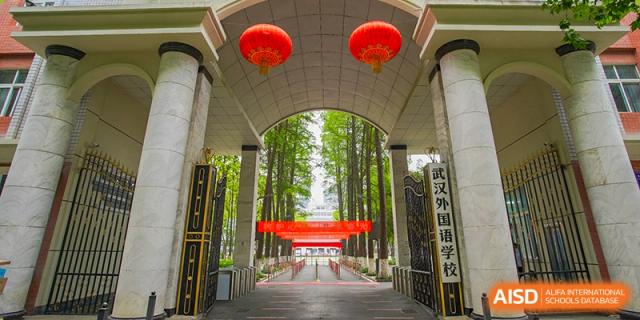 The main entrance gate of Wuhan Foreign Languages School International Division with arching greenery and red lanterns hanging above.