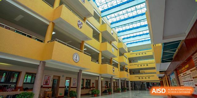 The interior of the bright, multi-level school building with yellow walls and a glass ceiling at Wuhan Foreign Languages School International Division.