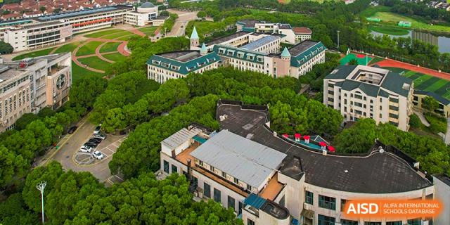 A high aerial view of the green, expansive campus of Wuhan Foreign Languages School International Division surrounded by trees.
