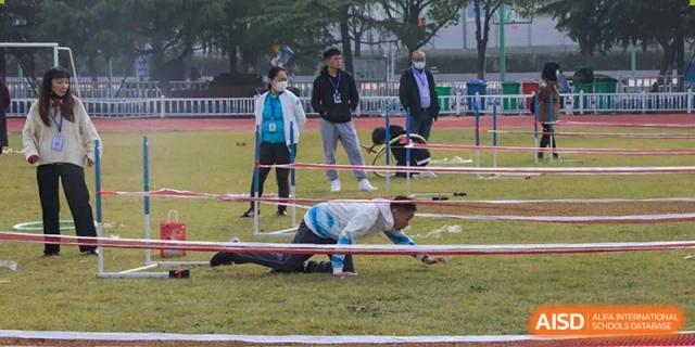 Students from Wuhan Foreign Languages School International Division competing in a fun, low-crawling race on the grass during field day.