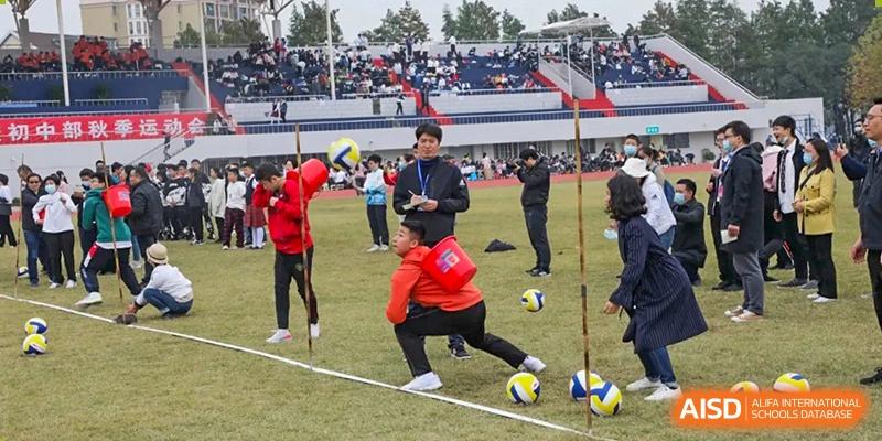 A student from Wuhan Foreign Languages School International Division crouches down while participating in a sports competition on the field with spectators in the background.