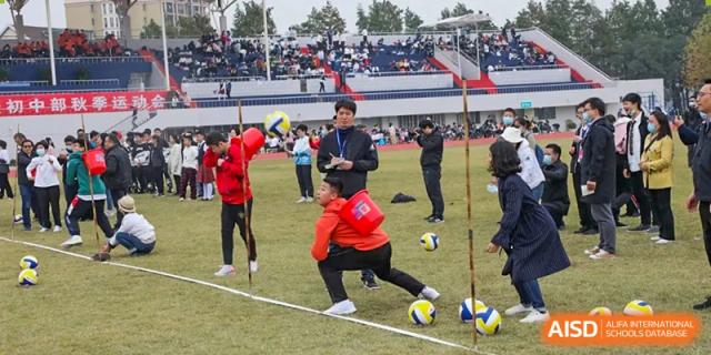 A student from Wuhan Foreign Languages School International Division crouches down while participating in a sports competition on the field with spectators in the background.