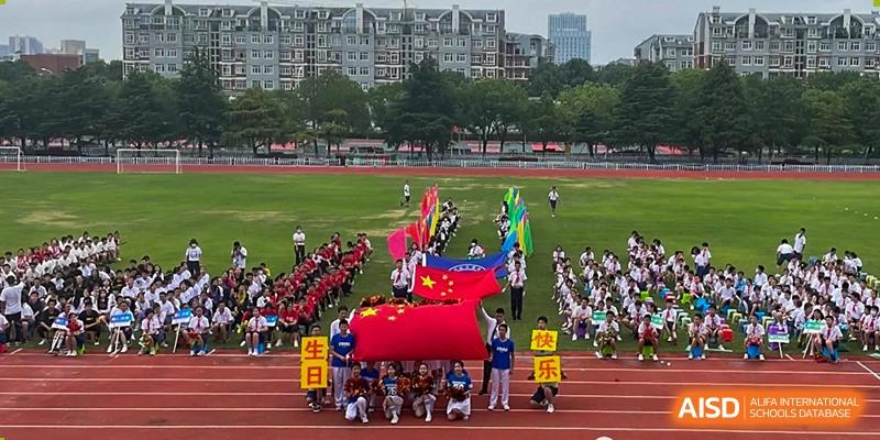 Students holding a large Chinese flag during a ceremony or parade on the sports field at Wuhan Foreign Languages School International Division.