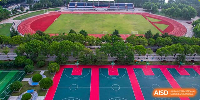 Aerial view of the outdoor basketball and sports courts with a red surface and surrounding green trees at Wuhan Foreign Languages School International Division.