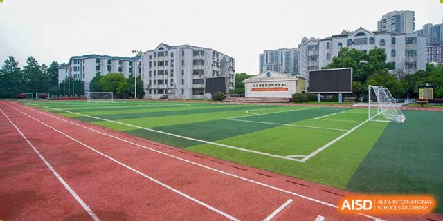 The outdoor running track and green turf field with a distant school building at Wuhan Foreign Languages School International Division.