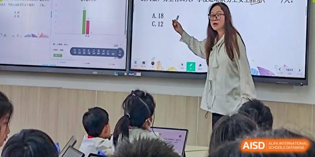 A teacher is pointing to a problem on a smart board while students are in a classroom at Shanghai Shangde Experimental School.