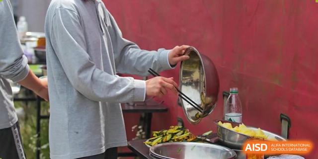A person is cooking in a large wok and holding a bowl of vegetables at Shanghai Shangde Experimental School.