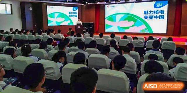 An audience of students from Tianjin Nankai High School  watching a presentation on a stage with a screen, from a different angle.