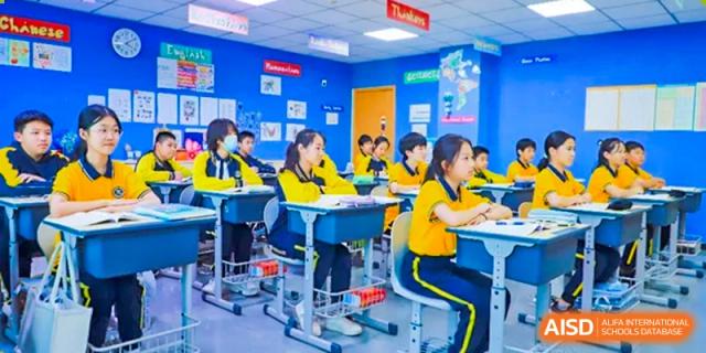 Students in yellow and blue uniforms from Beijing Xin Fuxue International Academy sit at desks in a classroom.