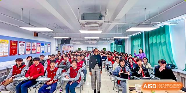 A large group of students at Beijing Xin Fuxue International Academy sit together in an auditorium or lecture hall.