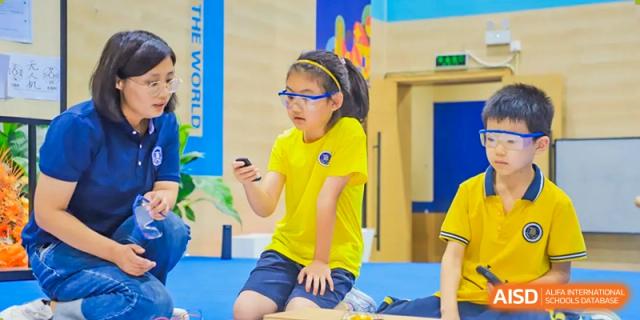 A student from Beijing Xin Fuxue International Academy looks at a small device while a teacher assists.