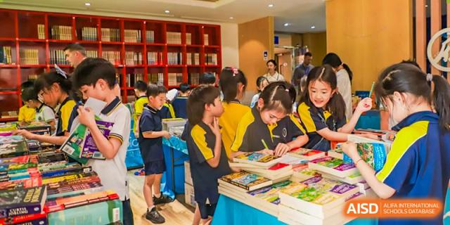 Students from Beijing Xin Fuxue International Academy are shown in a library or media center, looking at books and working on projects.