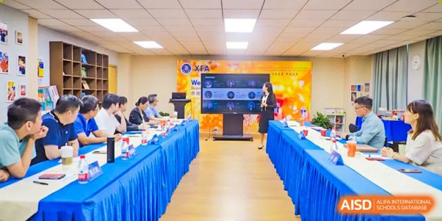 A long shot of a modern conference room or classroom at Beijing Xin Fuxue International Academy with a large screen and tables arranged for a meeting.