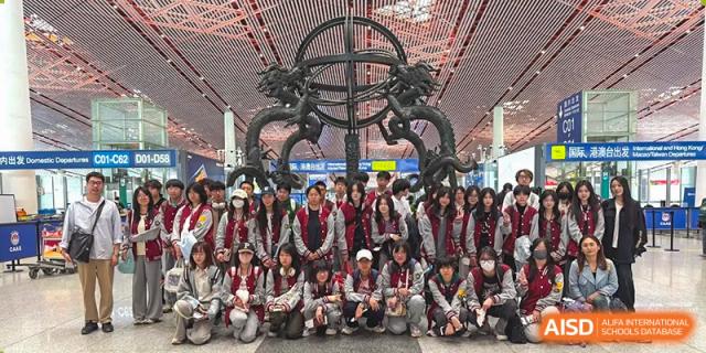 A large group of students and teachers from Beijing Xin Fuxue International Academy pose for a group photo in front of a unique structure.