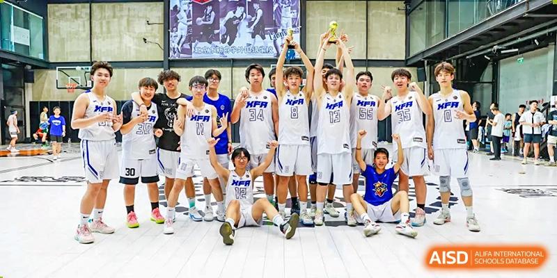 The boys' basketball team from Beijing Xin Fuxue International Academy celebrates their victory, holding a trophy and posing for a team photo.