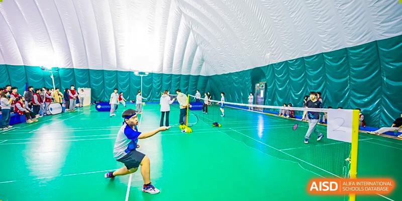 Two students from Beijing Xin Fuxue International Academy play badminton in an indoor gymnasium.
