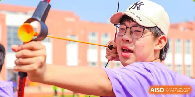 A student from Beijing Xin Fuxue International Academy focuses intently while practicing archery outdoors.
