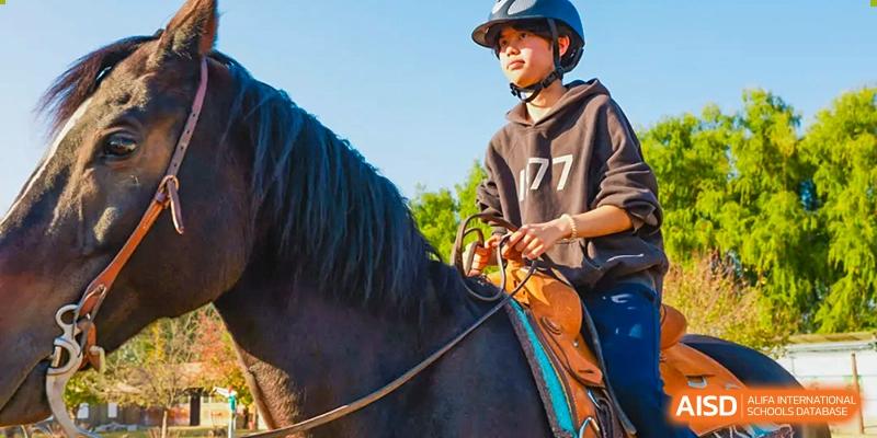 A student from Beijing Xin Fuxue International Academy is shown from the side while riding a horse.