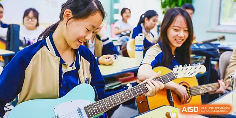 A female student from Beijing Xin Fuxue International Academy plays a guitar in a music classroom with other students.
