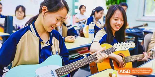 A female student from Beijing Xin Fuxue International Academy plays a guitar in a music classroom with other students.