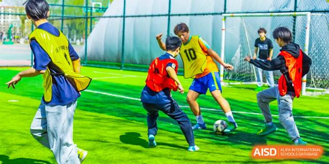 Students from Beijing Xin Fuxue International Academy play soccer on a sports field.