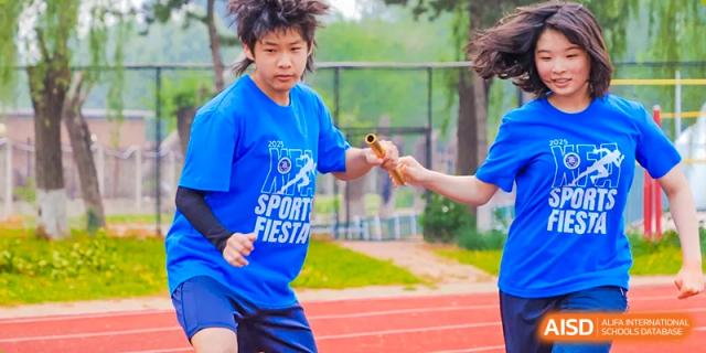 Two students from Beijing Xin Fuxue International Academy hand off a baton to each other during a track event.