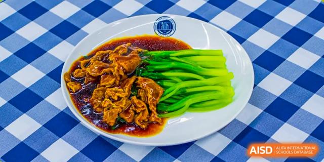 A plate of braised meat with fresh green vegetables, a dish available at Beijing Xin Fuxue International Academy.