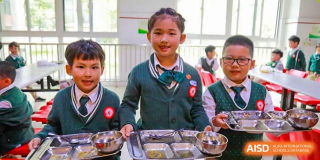 A young girl smiles while holding a tray of food in the cafeteria, at Changshu Lunhua Foreign Language School.