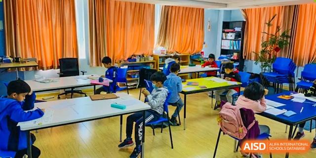 A male student with a backpack sitting at a table and drawing in a classroom at the Qingdao Amerasia International School.