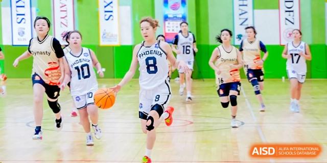 A female student in a basketball uniform dribbling the ball down the court during a game at the Qingdao Amerasia International School.