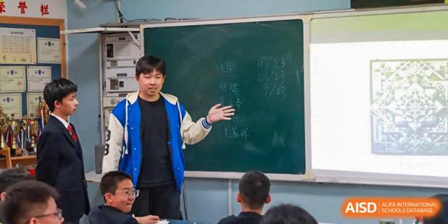 A student from Xi'an Jiaotong-Liverpool University Affiliated School (XJTLU-AS) is giving a presentation in front of a classroom blackboard.