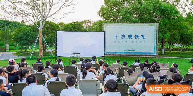Students from Xi'an Jiaotong-Liverpool University Affiliated School (XJTLU-AS) watch a presentation on a large screen outdoors.