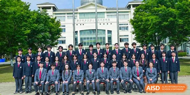 A group of students from Xi'an Jiaotong-Liverpool University Affiliated School (XJTLU-AS) are posing for a formal class photo in front of a school building.