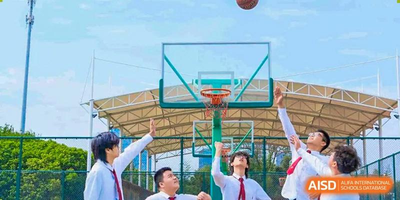 A group of students from Xi'an Jiaotong-Liverpool University Affiliated School (XJTLU-AS) playing basketball on an outdoor court. One student is in the middle of a jump shot.