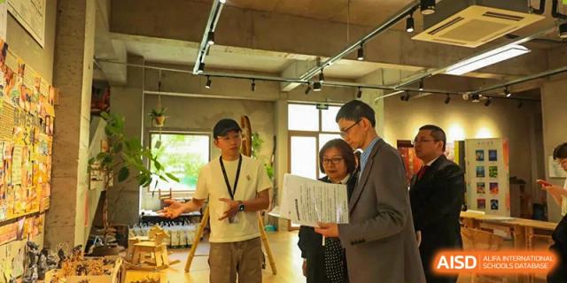 A student from Xi'an Jiaotong-Liverpool University Affiliated School (XJTLU-AS) presents a document to an adult in a school hallway.