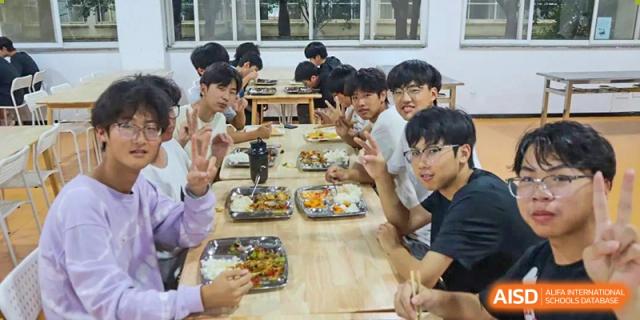 A group of students from Xi'an Jiaotong-Liverpool University Affiliated School (XJTLU-AS) eating a meal together at a long table.