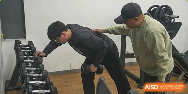 A student from Xi'an Jiaotong-Liverpool University Affiliated School (XJTLU-AS) is lifting a dumbbell with a trainer's assistance.