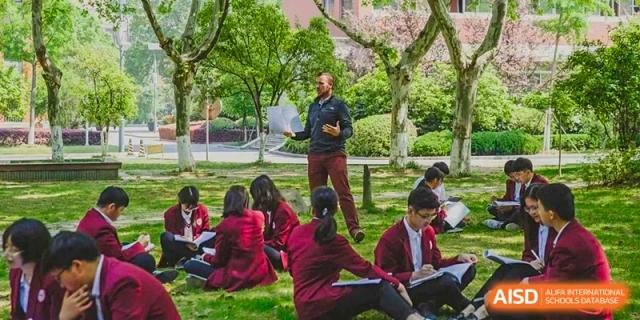 A male teacher instructing a group of students seated outdoors on the grass in a casual lesson at Wuxi No.1 High School.