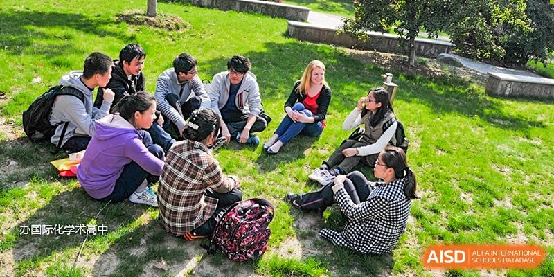 A group of high school students sitting and relaxing on a grassy slope outdoors, chatting and enjoying the sunny weather at Wuxi No.1 High School.