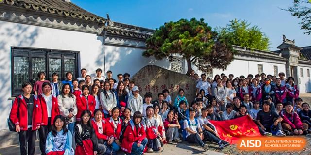 A large group of students in red uniforms gathered for a group photo outdoors near a traditional rock sculpture at Wuxi No.1 High School.