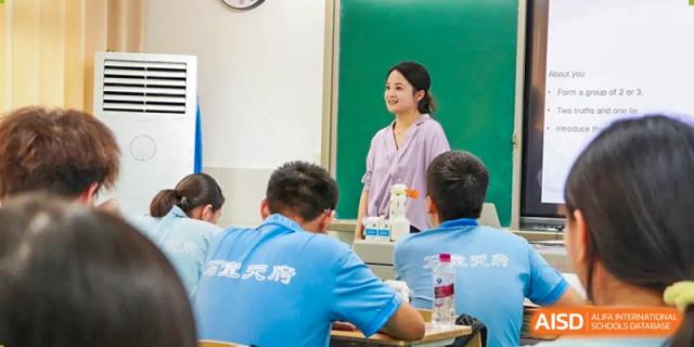 A teacher in a pink shirt standing and talking with a student at his desk in a classroom. Chengdu Shishi Tianfu High School International Department.