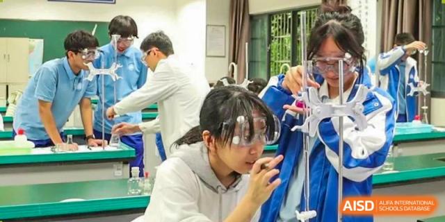 A student wearing safety goggles and a white lab coat observing a reaction in a beaker. Chengdu Shishi Tianfu High School International Department.