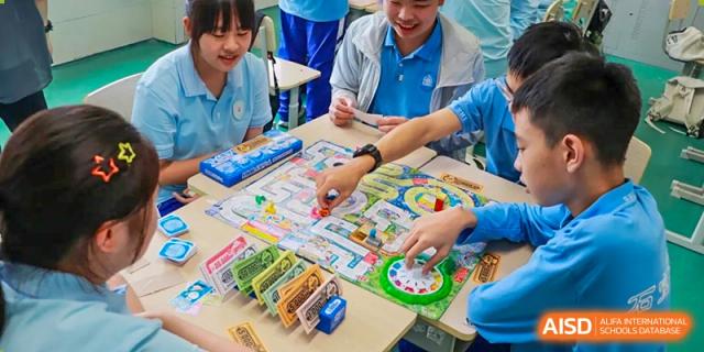 A group of students and a teacher gathered around a table with a board game, with one student's hand on a spinner. Chengdu Shishi Tianfu High School International Department.