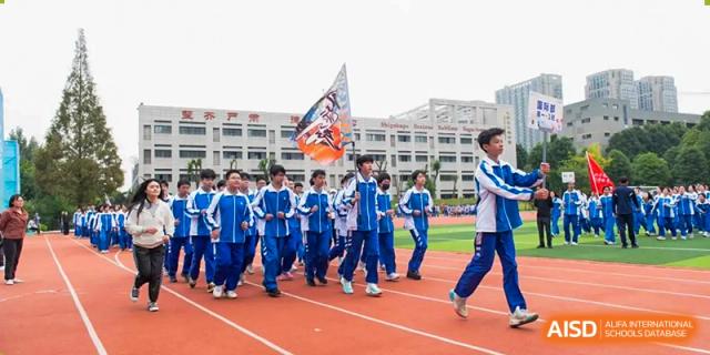 A group of students in blue tracksuits marching with a flag on a running track. Chengdu Shishi Tianfu High School International Department.